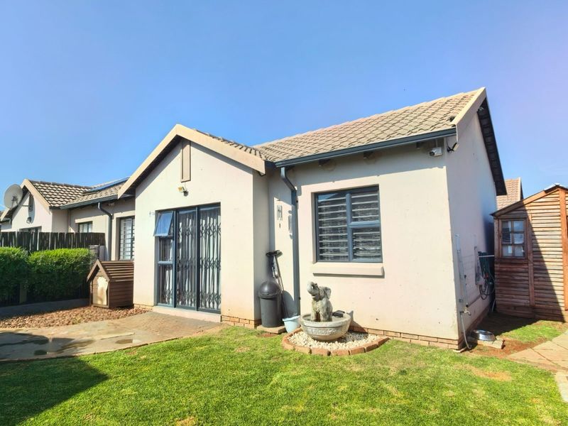 Rear view of the townhouse featuring a private garden, paved patio area, sliding glass doors with security gates, and a tiled roof.