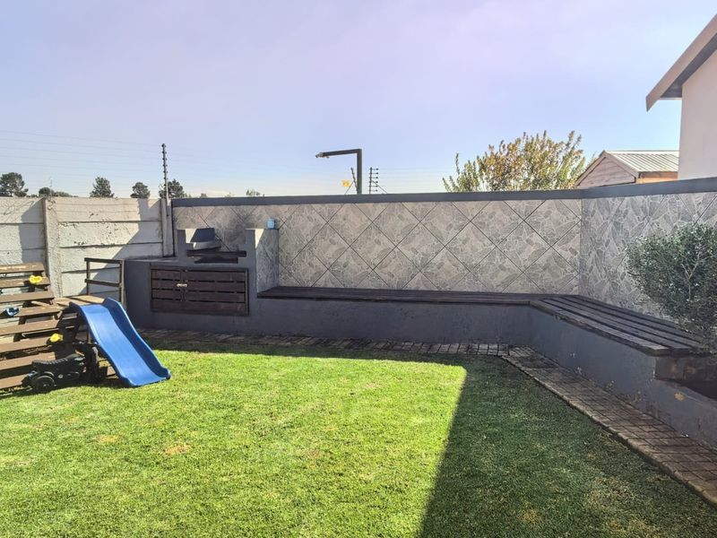 A private rear garden featuring a built-in braai area, integrated bench seating with stone-tiled feature wall, and a well-maintained lawn.