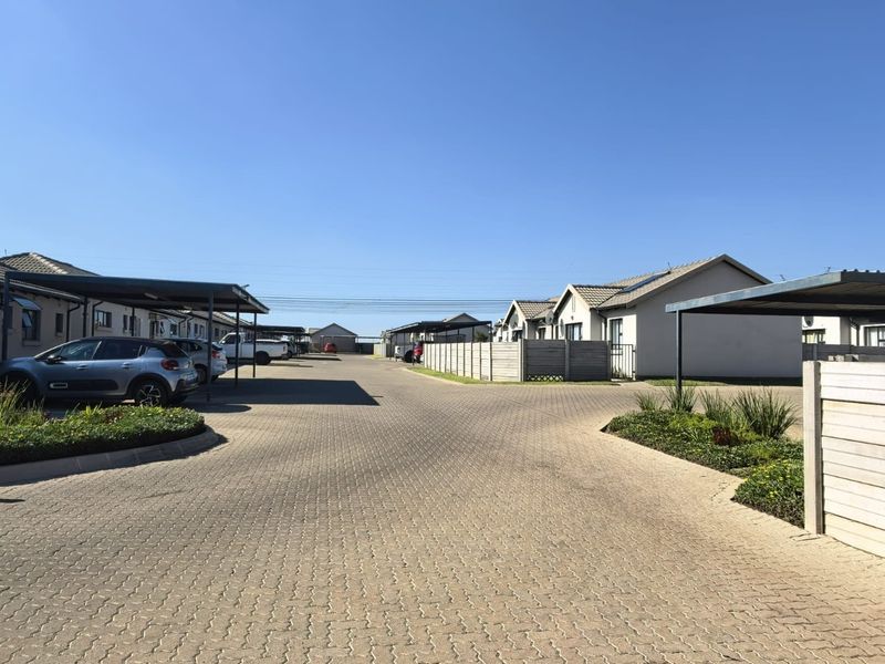 A view of the townhouse complex driveway featuring paved roads, covered parking bays, and perimeter boundary walls.