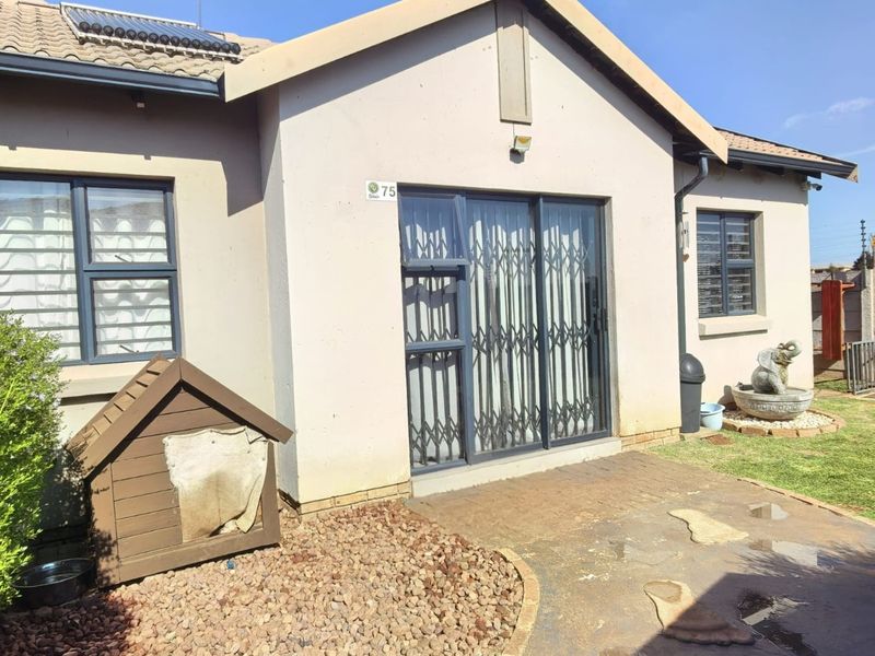 Rear view of the townhouse featuring a paved patio area, sliding glass doors with security gates, and a solar water heating system on the roof.