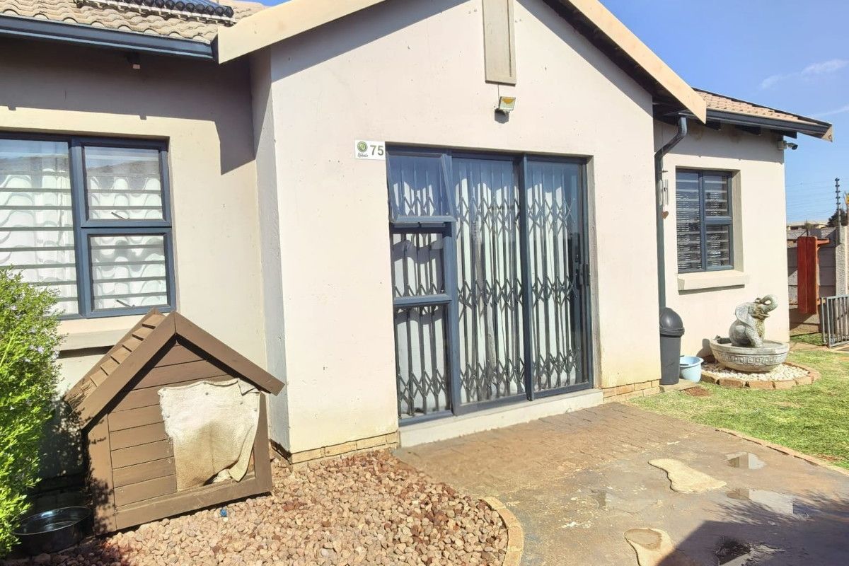 Rear view of the townhouse featuring a paved patio area, sliding glass doors with security gates, and a solar water heating system on the roof.