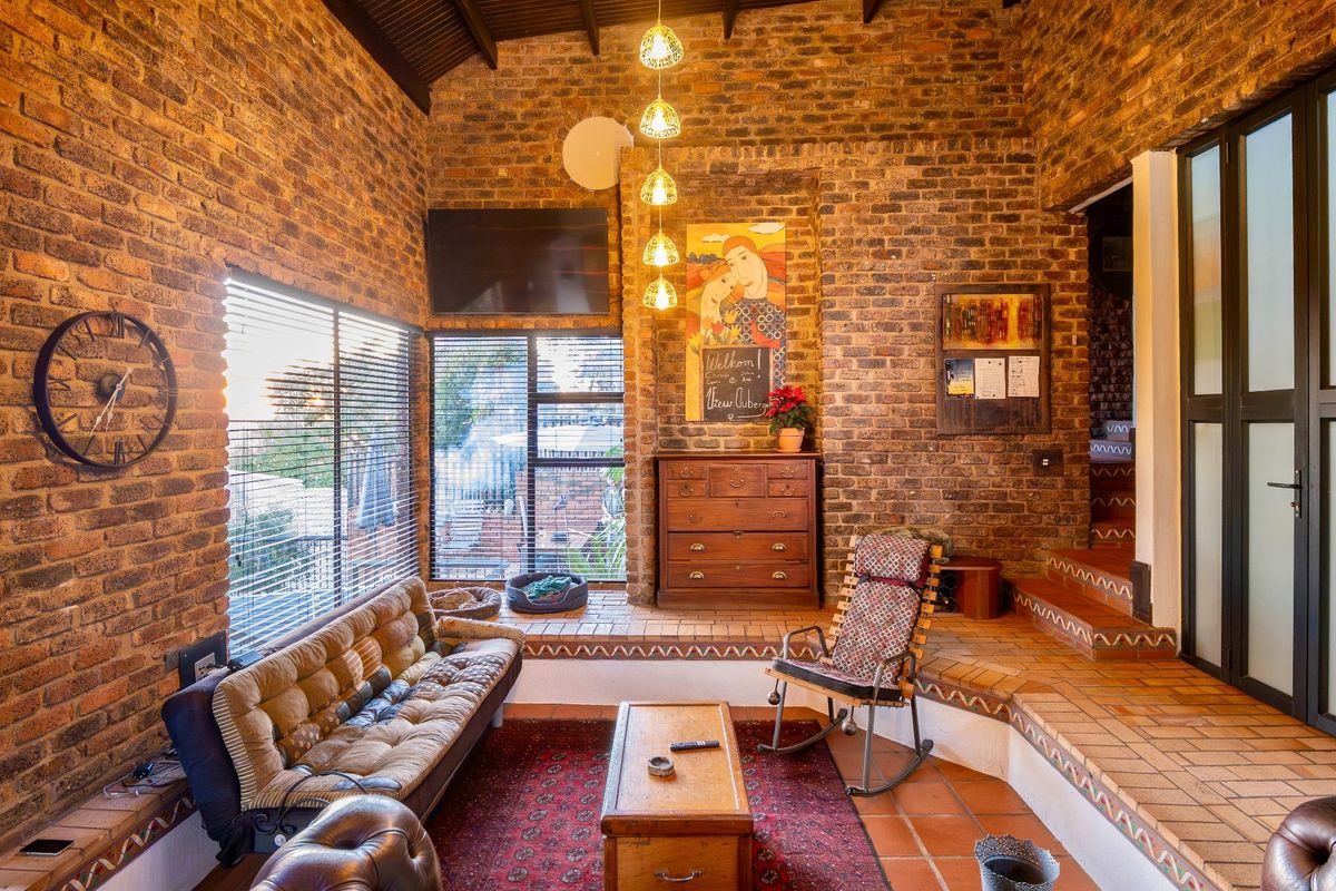 A rustic living room featuring exposed brick walls, high vaulted timber ceilings, and terracotta tiled flooring with a built-in brick bench.