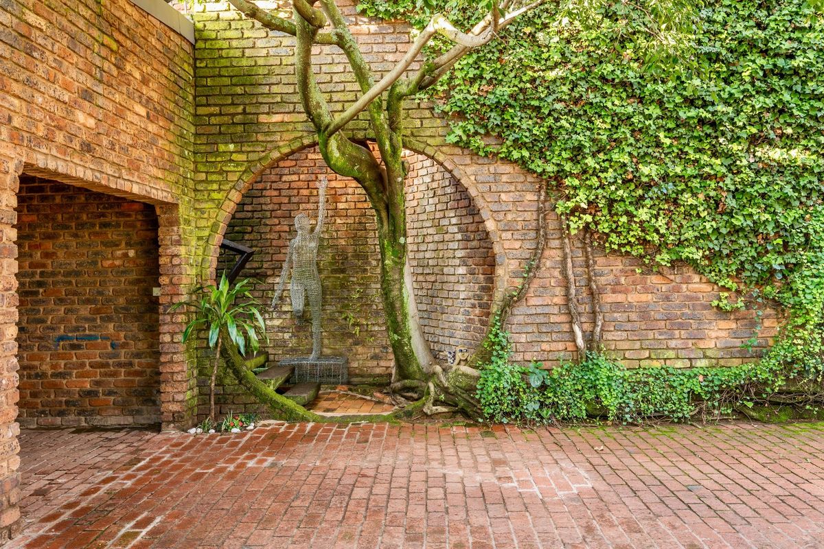 A charming, rustic courtyard featuring exposed brick walls, a circular architectural archway, and mature tree integration with paved brick flooring.