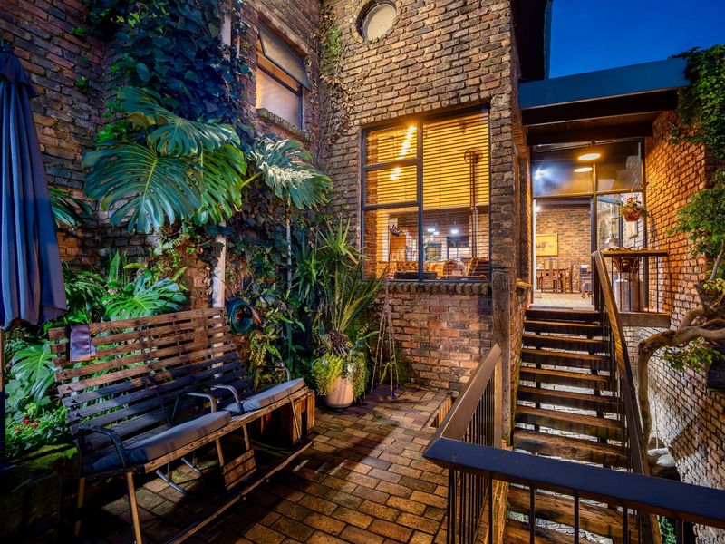 A charming, rustic brick-walled patio area featuring a staircase, integrated lighting, and lush greenery, creating an inviting outdoor entertainment space.