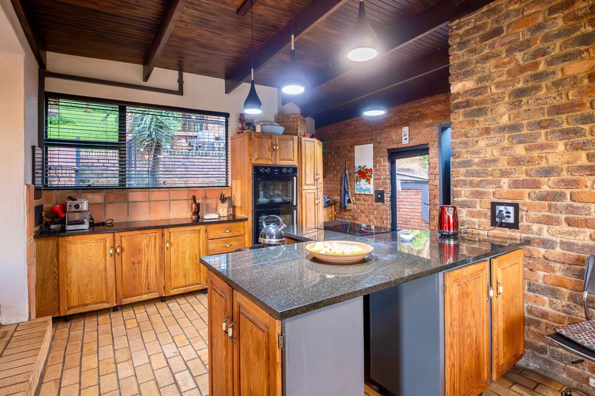 A rustic kitchen featuring exposed brick walls, timber-clad ceiling, granite countertops, and a central island with built-in cabinetry.