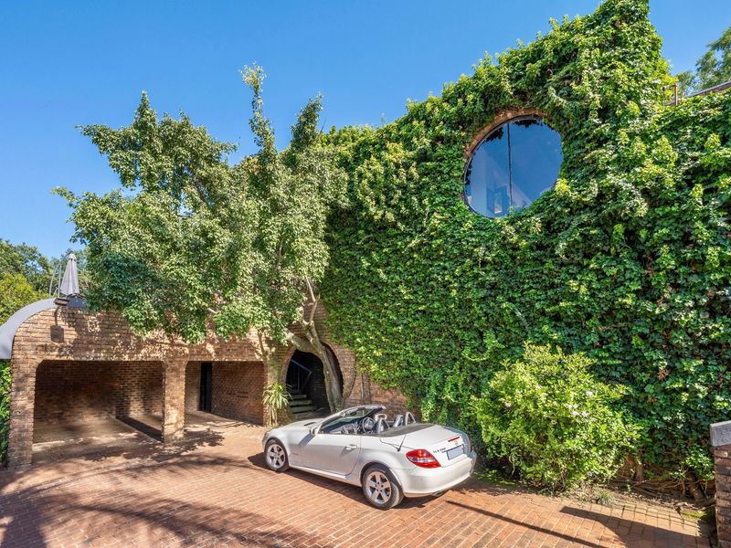 A unique architectural facade featuring extensive ivy coverage, a distinctive circular window, and a covered brick carport area.