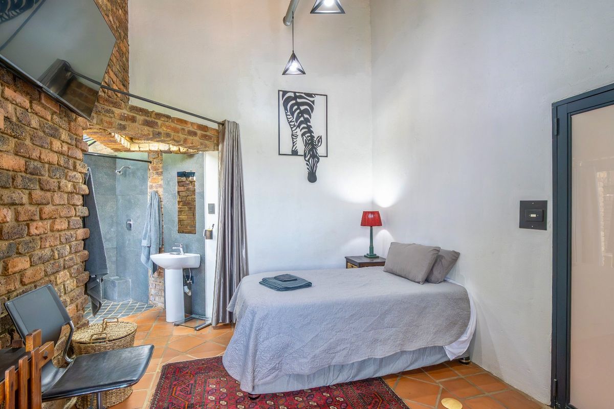 A bedroom featuring exposed brick walls, terracotta floor tiles, and an open-plan en-suite bathroom with a pedestal basin and shower.