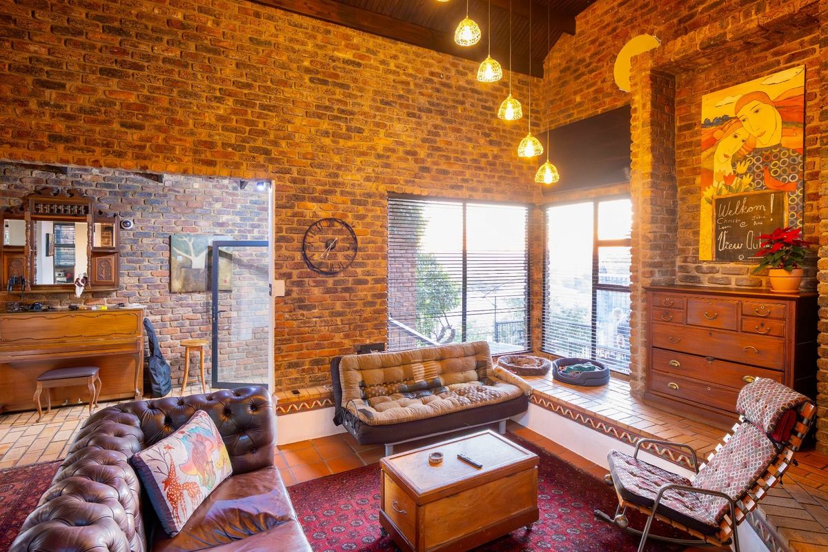 Spacious living room featuring exposed brick walls, high timber-beamed ceilings, terracotta floor tiles, and large windows with integrated blinds.