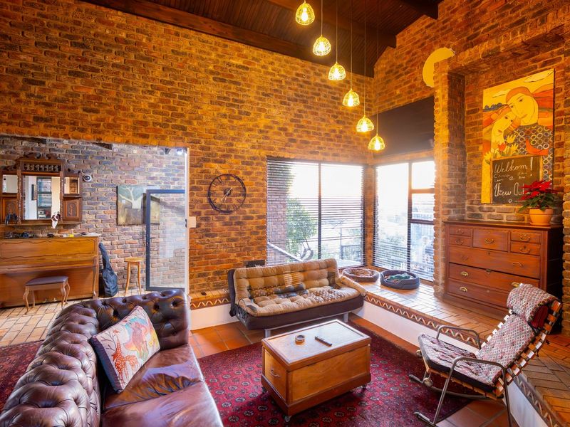 Spacious living room featuring exposed brick walls, high timber-beamed ceilings, terracotta floor tiles, and large windows with integrated blinds.