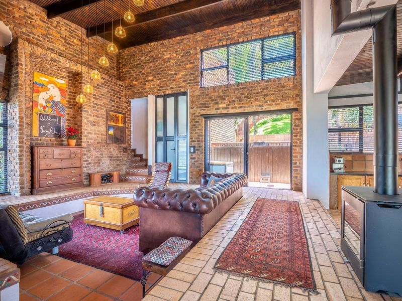 Spacious open-plan living area featuring exposed brick walls, high timber-beamed ceilings, a wood-burning fireplace, and large sliding doors leading to the outdoor space.