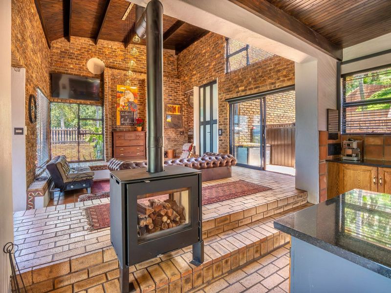 Open-plan living area featuring exposed brick walls, timber-clad vaulted ceilings, a central freestanding fireplace, and seamless flow to the outdoor patio area.