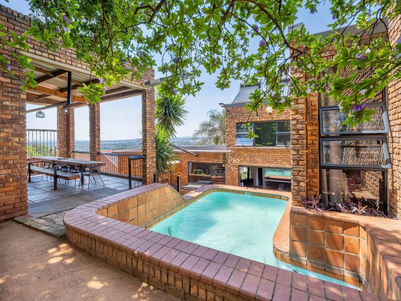 A spacious outdoor entertainment area featuring a built-in swimming pool, covered patio with brick pillars, and scenic elevated views.