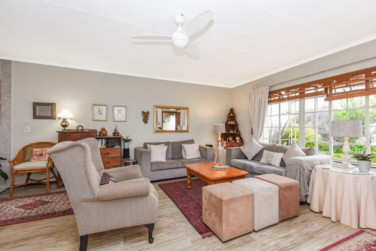 A comfortable living room featuring wood-look tile flooring, a ceiling fan, and large windows providing natural light and garden views.