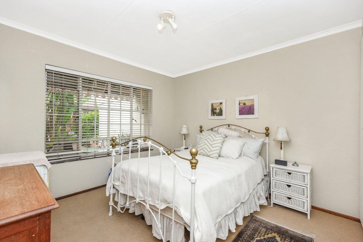 A well-lit bedroom featuring neutral wall tones, carpeted flooring, and a window with fitted blinds overlooking the exterior.