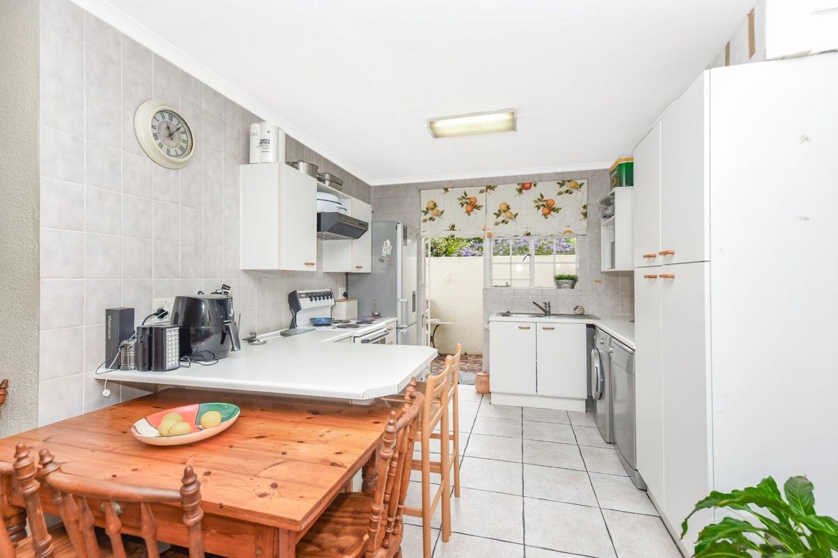 Functional kitchen featuring white cabinetry, tiled splashbacks, built-in stove, and integrated laundry space with direct access to an outdoor area.