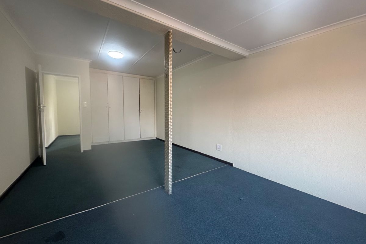 An empty bedroom featuring built-in cupboards, a central structural support column, and blue carpeting, offering a blank canvas for renovation.