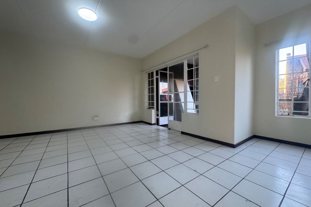 An empty living room featuring white ceramic floor tiles, large windows with security bars, and a glass sliding door leading to an outdoor area.