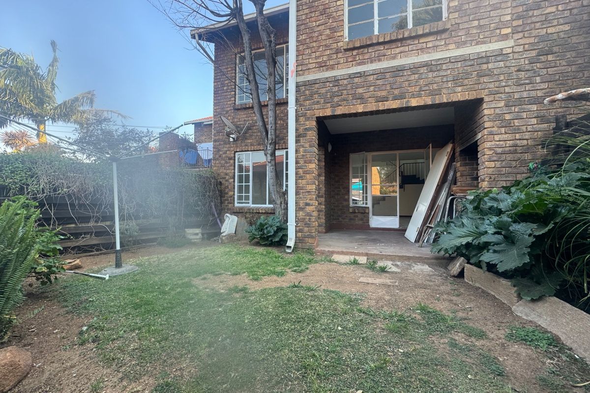 Rear view of a double-story brick apartment building featuring a covered patio area and a private garden space.