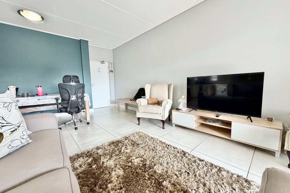 A bright living room featuring tiled flooring, a neutral color palette, and a dedicated workspace area with a feature wall.