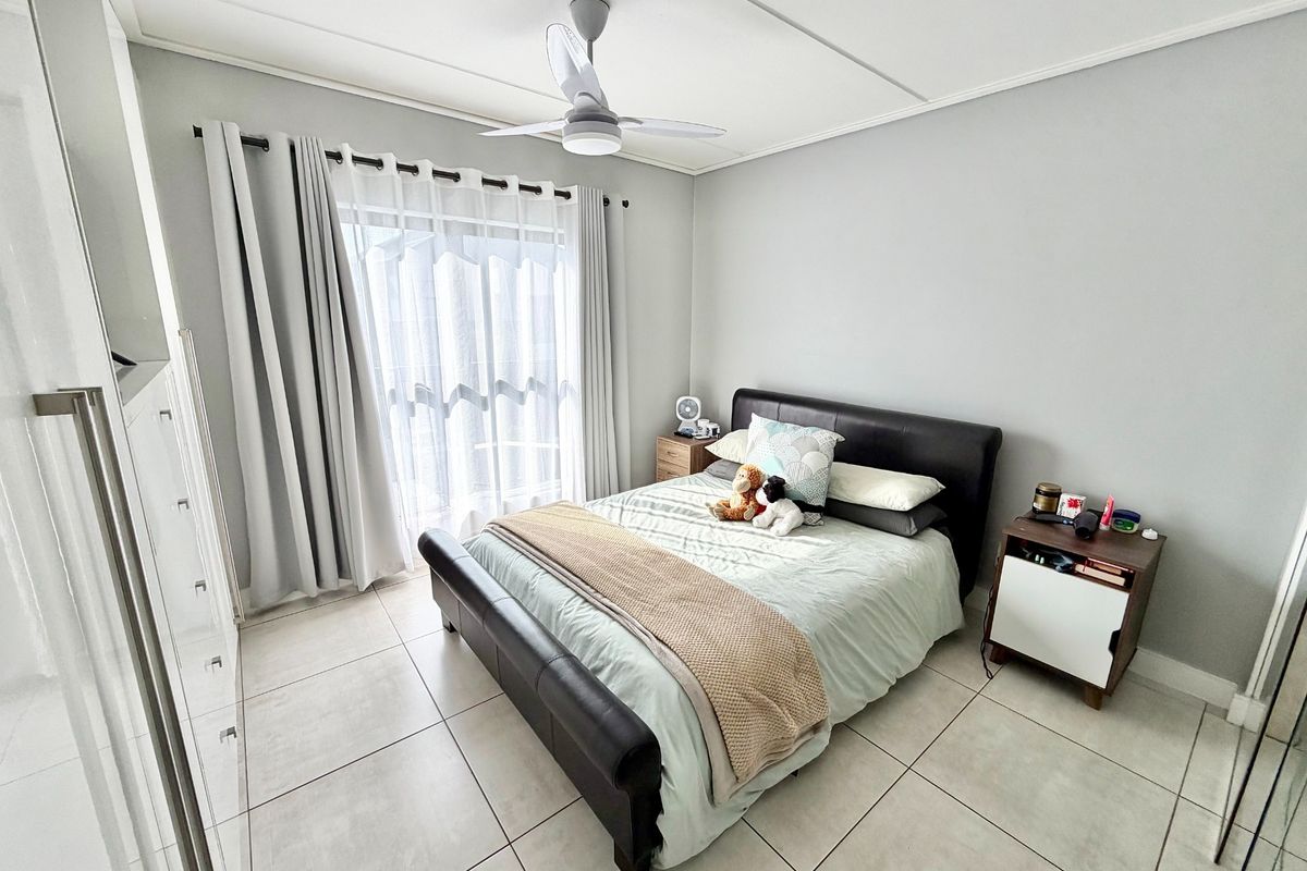 A well-lit bedroom featuring large format floor tiles, a ceiling fan, and sliding glass doors leading to an outdoor area.