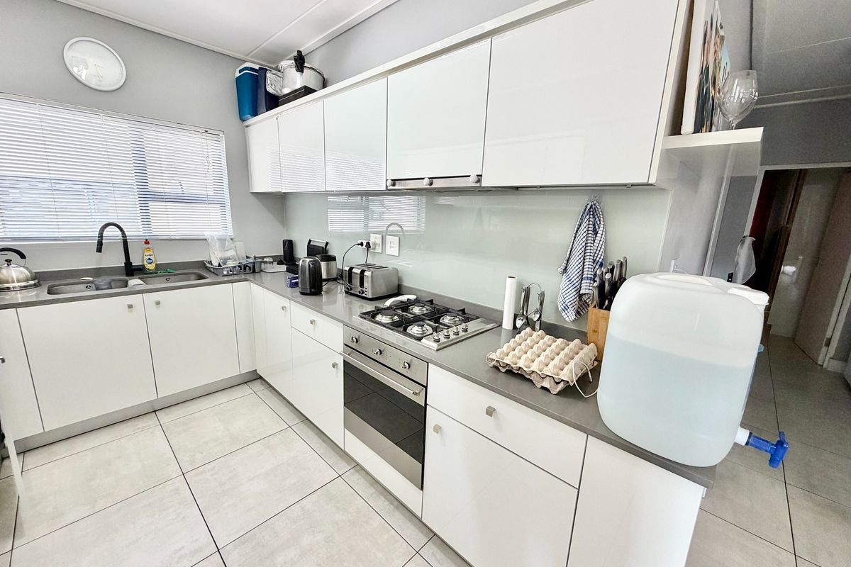 Modern kitchen featuring white high-gloss cabinetry, stone-look countertops, a built-in gas hob, stainless steel oven, and a sleek glass splashback.