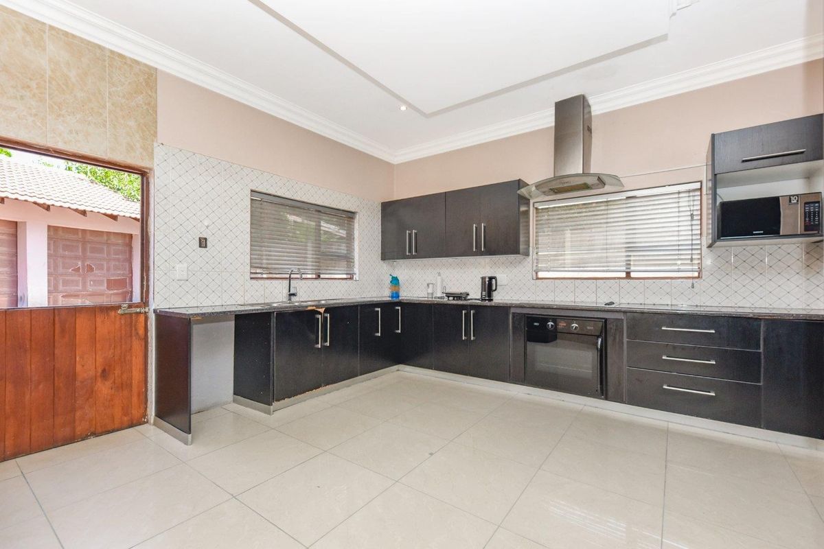A functional kitchen featuring dark cabinetry, granite countertops, a built-in oven, extractor fan, and tiled flooring with direct access to the exterior.