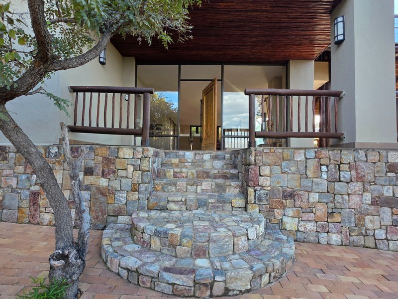 A charming entrance featuring natural stone cladding, rustic timber railings, and a covered patio area leading into the home.