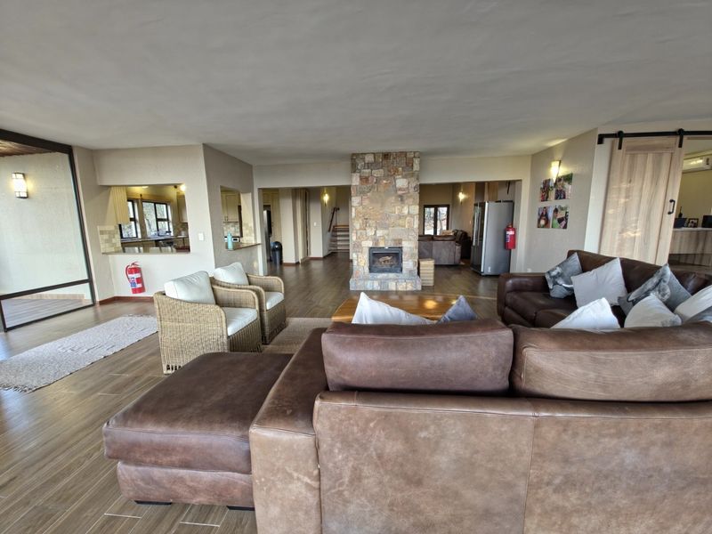 Spacious open-plan living area featuring a central stone-clad fireplace, wood-look tiled flooring, and a pass-through window connecting to the kitchen.