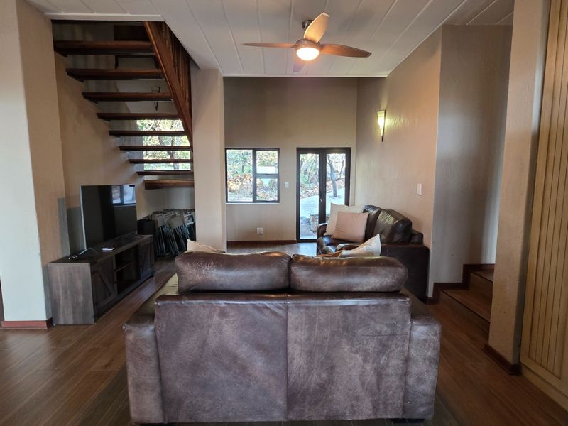 Open plan living area featuring wood-look flooring, a timber staircase, ceiling fan, and direct access to the outdoor area through glass doors.