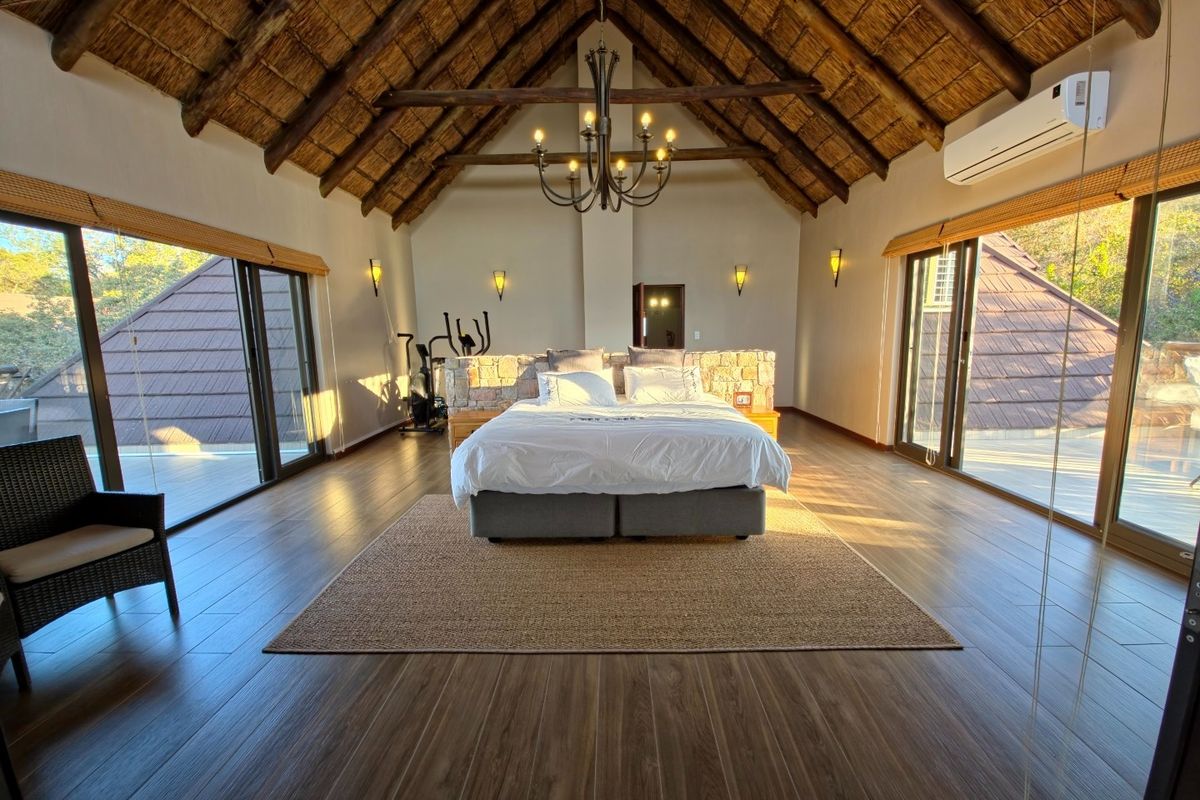 Spacious bedroom featuring a high vaulted thatched ceiling, exposed timber beams, wood-look flooring, and large sliding glass doors opening to an outdoor area.