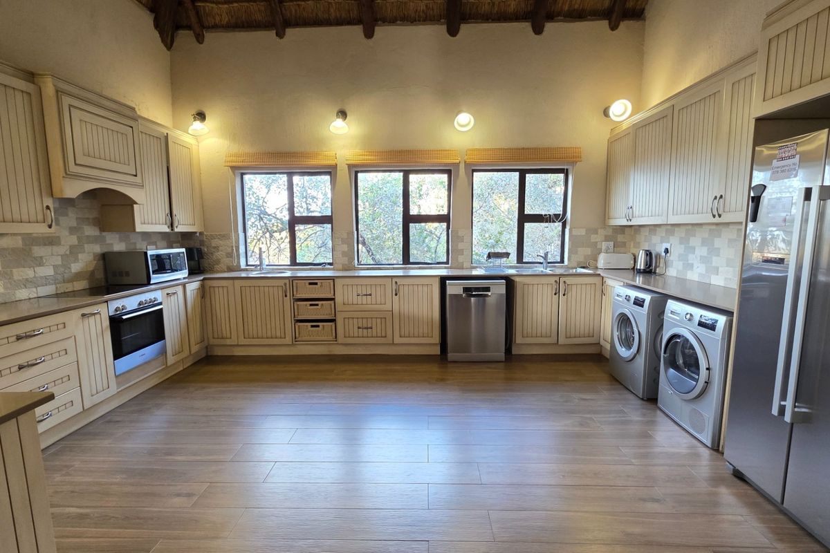 Spacious kitchen featuring light-toned cabinetry, tiled backsplash, integrated appliances, and large windows with natural light, set under a high vaulted ceiling.