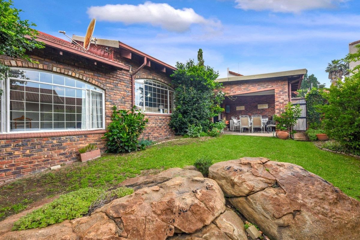 A private rear garden featuring a covered patio area, established lawn, and natural rock landscaping, set against a classic brick townhouse exterior.