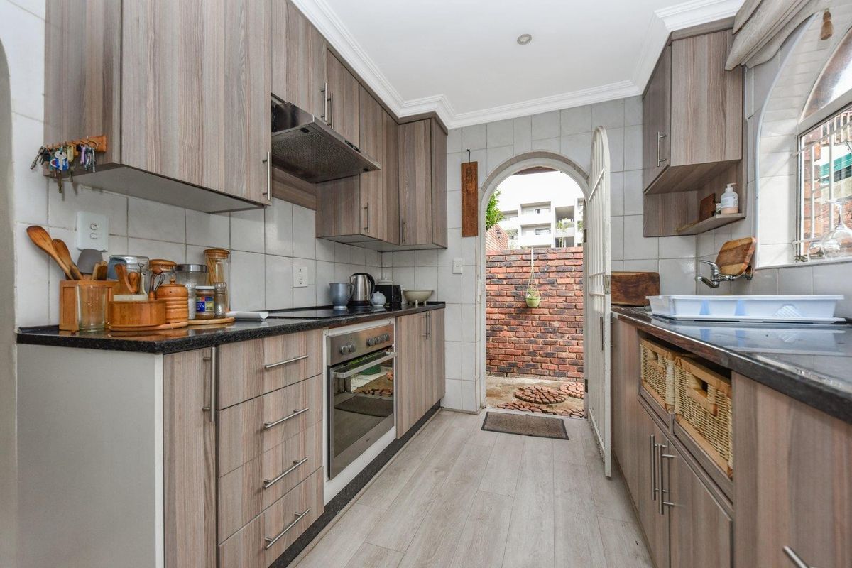 A functional galley-style kitchen featuring wood-look cabinetry, dark countertops, a built-in oven, extractor fan, and direct access to an enclosed rear courtyard.