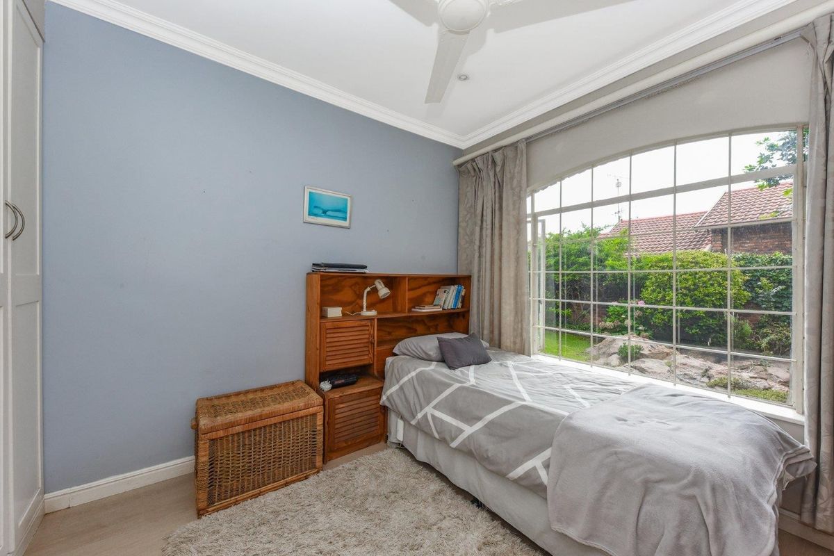 A bedroom featuring a large arched window with garden views, built-in cabinetry, and a ceiling fan.