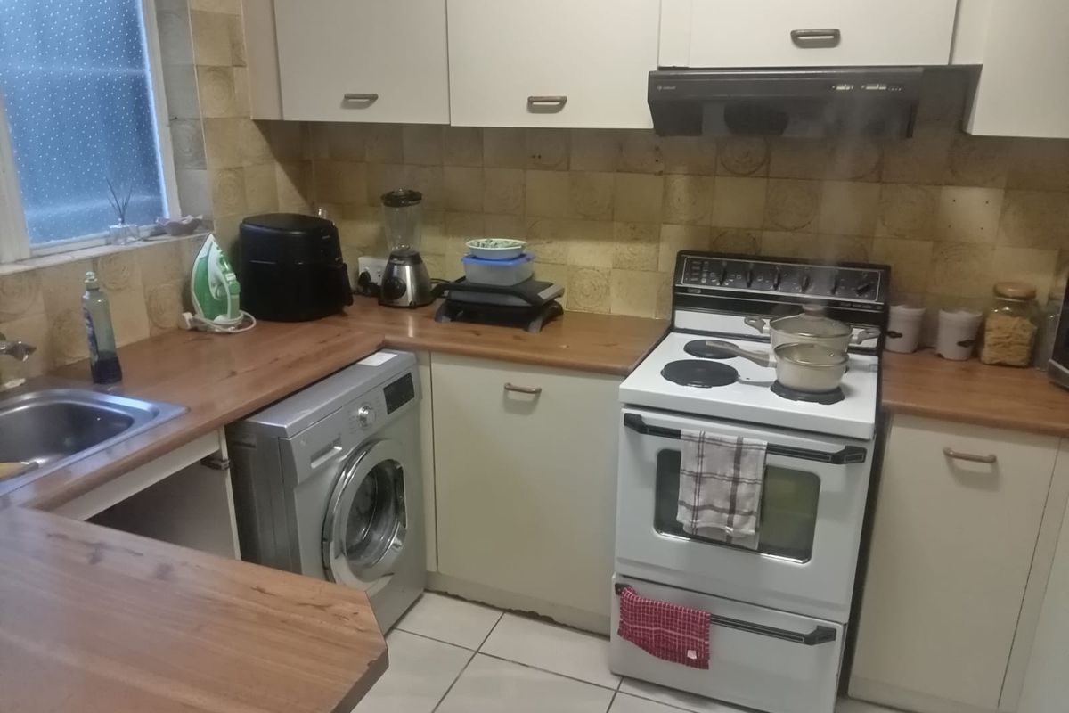 A functional kitchen featuring light-toned cabinetry, wood-look laminate countertops, a built-in oven with extractor fan, and integrated laundry plumbing.