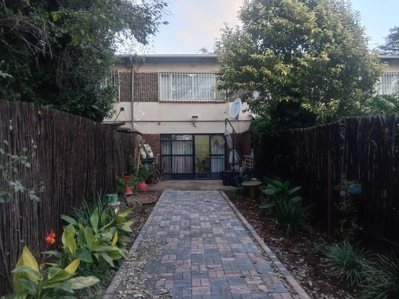 Rear view of the apartment featuring a paved walkway leading to the entrance, enclosed by natural reed fencing and established garden beds.