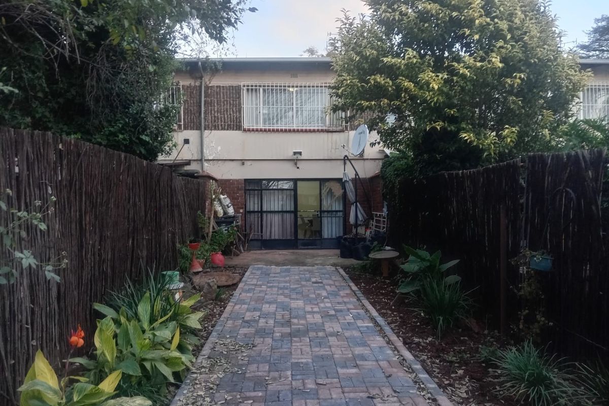 Rear view of the apartment featuring a paved walkway leading to the entrance, enclosed by natural reed fencing and established garden beds.