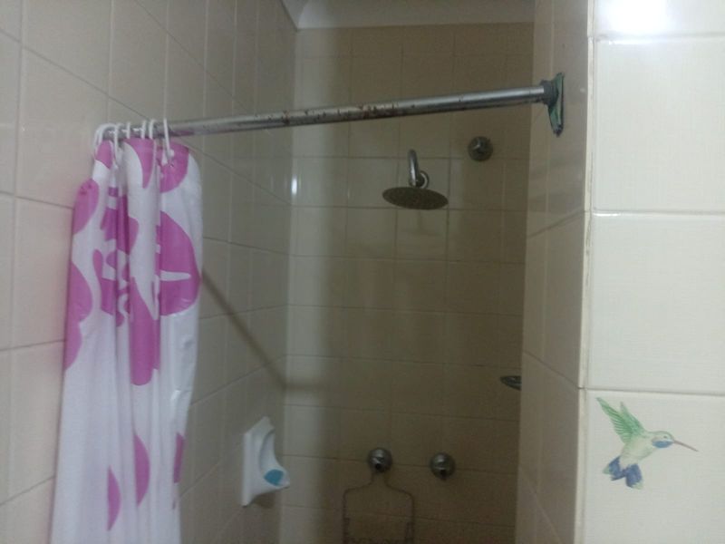 A dated shower area featuring wall-mounted shower head, chrome controls, and tiled surround.
