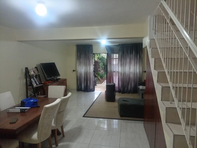 Open plan living and dining area featuring tiled flooring and a staircase with a metal balustrade, leading out to a rear garden space.