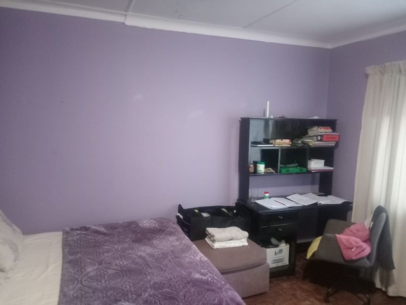 A bedroom featuring purple painted walls, parquet flooring, and a window with fitted curtains.