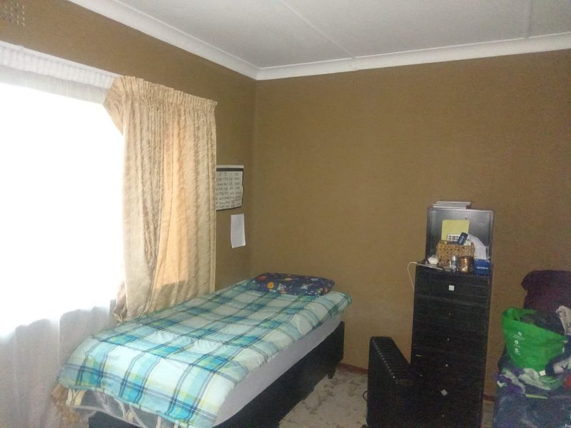 A bedroom featuring brown painted walls, a window with curtains, and a standard ceiling with cornice detailing.