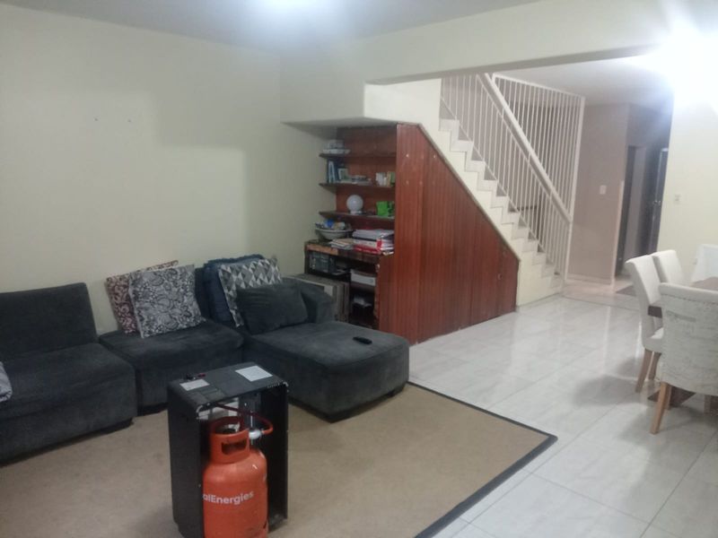 Open plan living area featuring tiled flooring and a built-in wooden staircase storage unit, providing a functional and versatile space.
