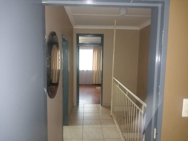 A view through a hallway featuring tiled flooring and a metal balustrade, leading towards a bedroom with natural light.