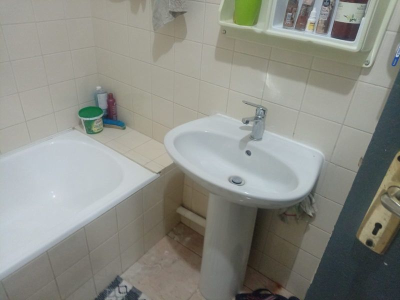 A functional bathroom featuring a white pedestal sink, a built-in bathtub with tiled surround, and wall-mounted storage shelving.