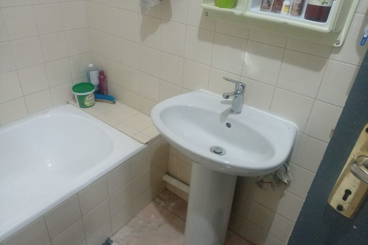 A functional bathroom featuring a white pedestal sink, a built-in bathtub with tiled surround, and wall-mounted storage shelving.