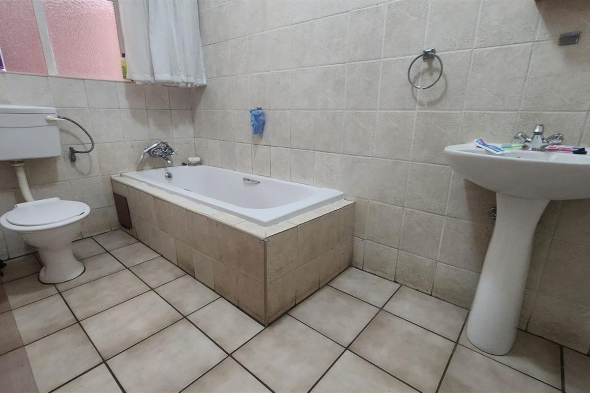A functional bathroom featuring a built-in bathtub, pedestal basin, and toilet with neutral wall and floor tiling.