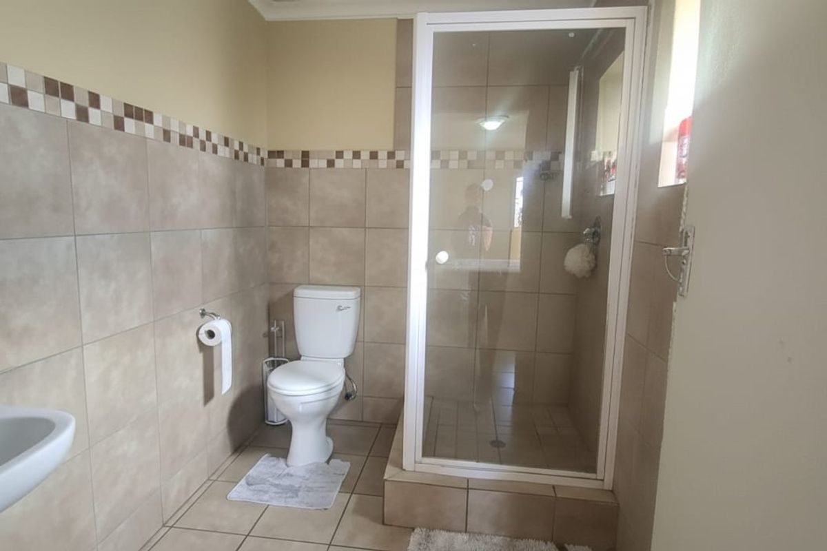 A functional bathroom featuring a walk-in shower with a glass enclosure, a standard toilet, and wall-mounted basin with tiled splashbacks.