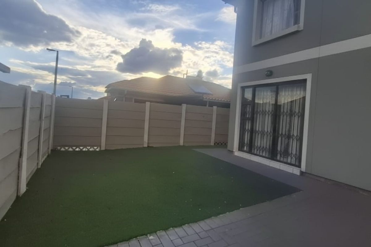 A private rear garden featuring a paved patio area, artificial lawn, and perimeter boundary walling, accessible via sliding glass doors.