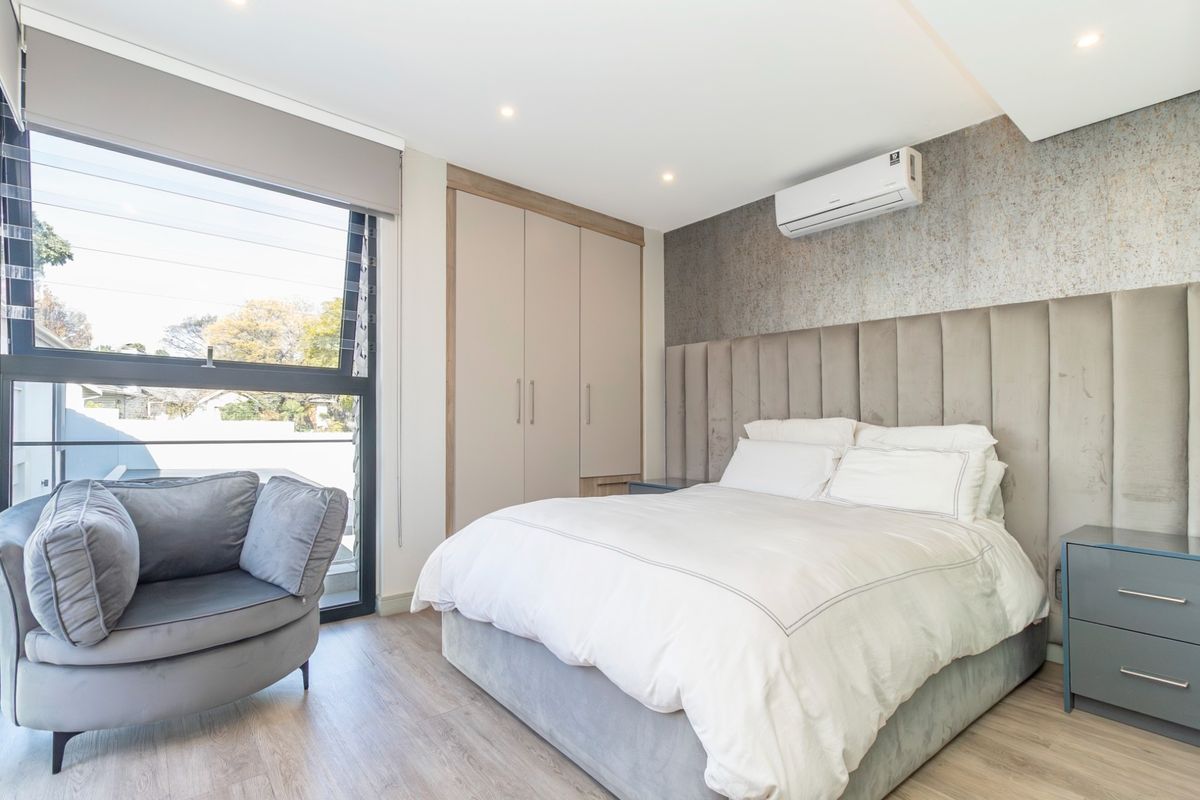 Modern bedroom featuring built-in wardrobes, a wall-mounted air conditioning unit, and large windows providing natural light.