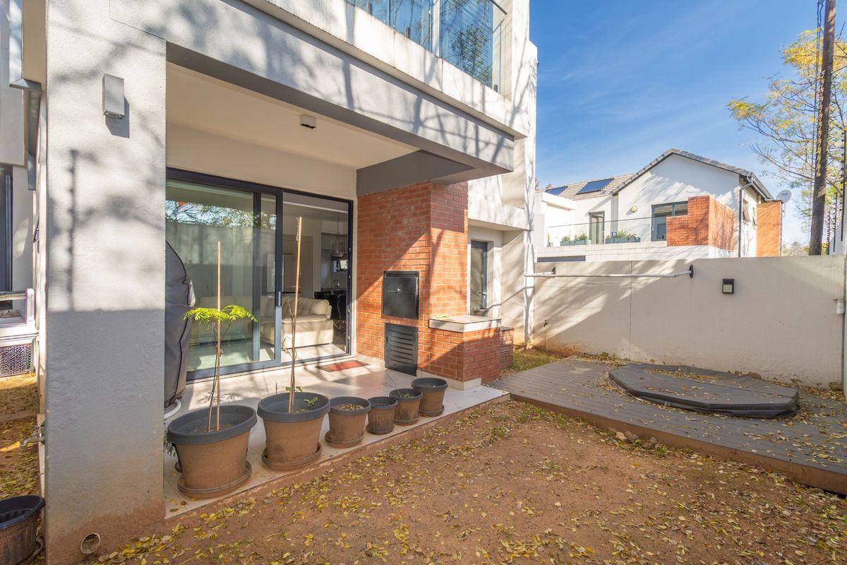 A private rear patio area featuring a built-in brick braai, sliding glass doors, and a small wooden deck with an integrated spa cover.